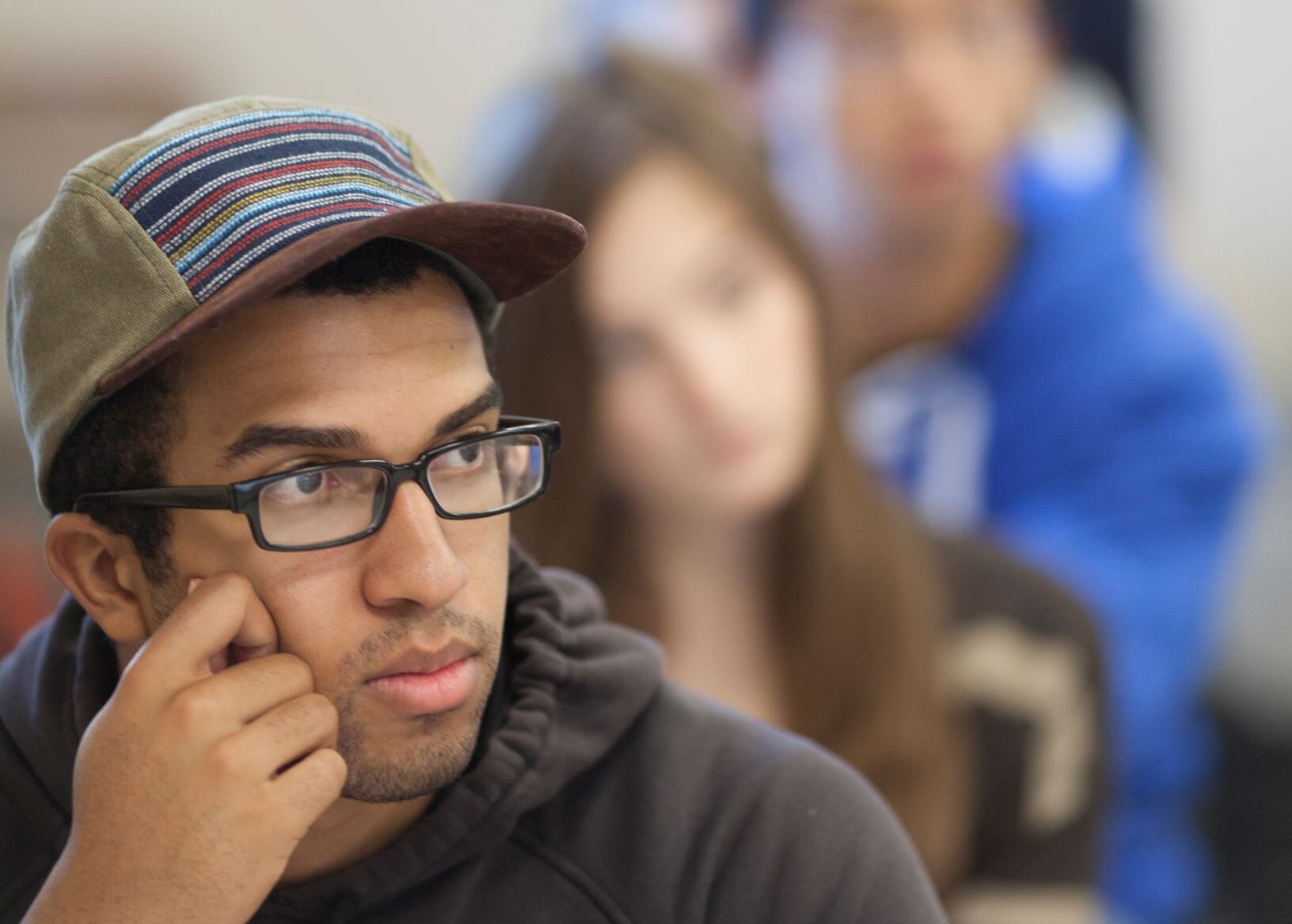 student leans on hand listening in class, other students out of focus also listen behind him