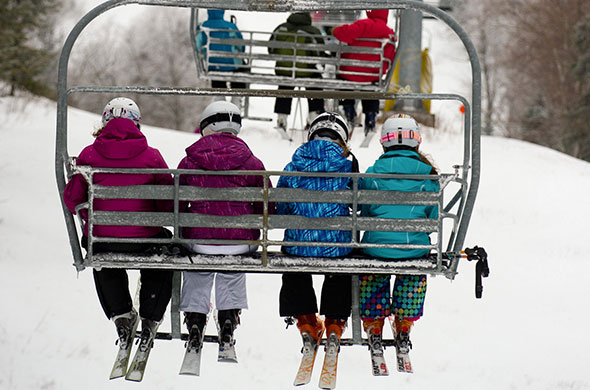 Skiers sit on chair lift going up the ski mountain. 