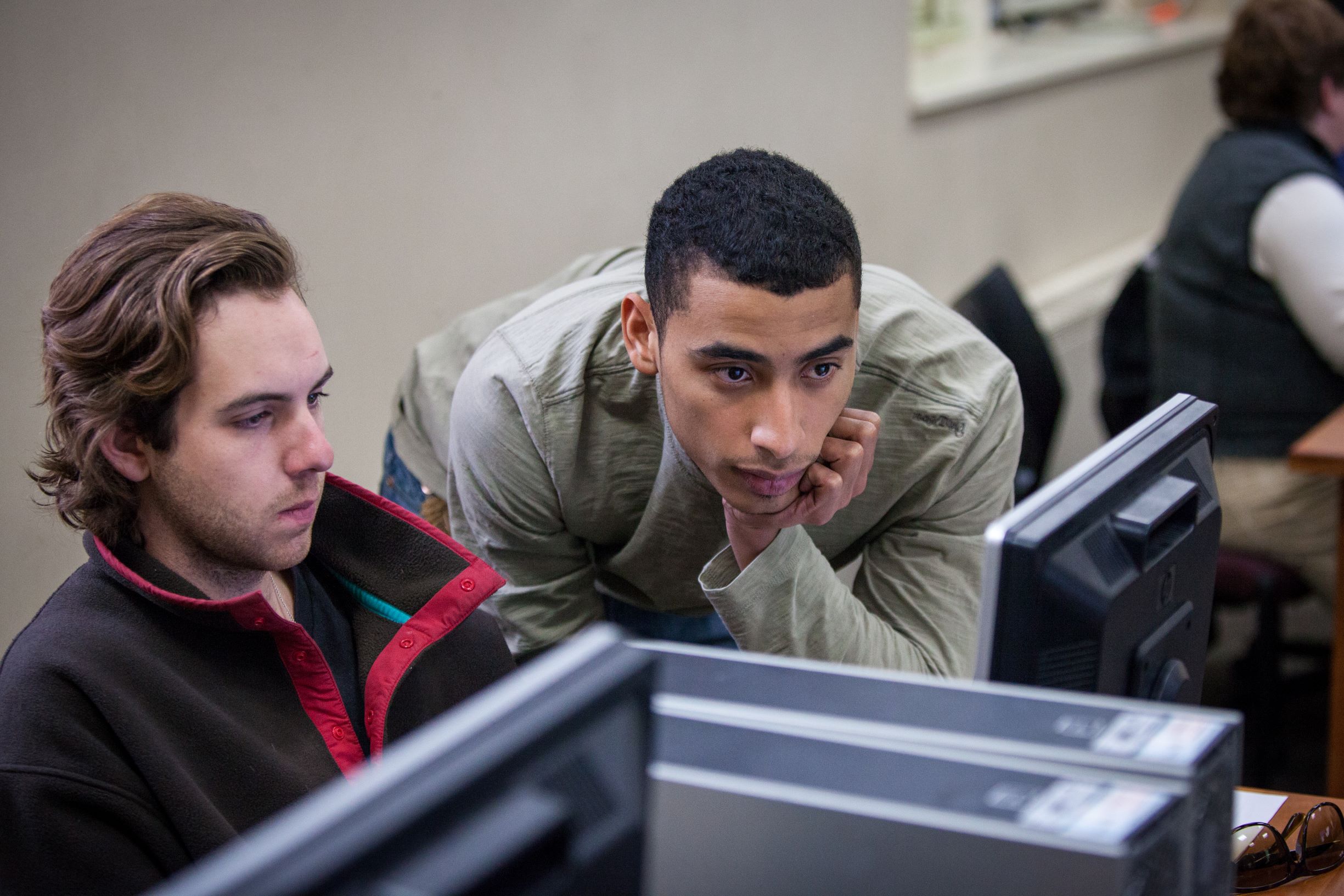 Two male students look together at a computer monitor.