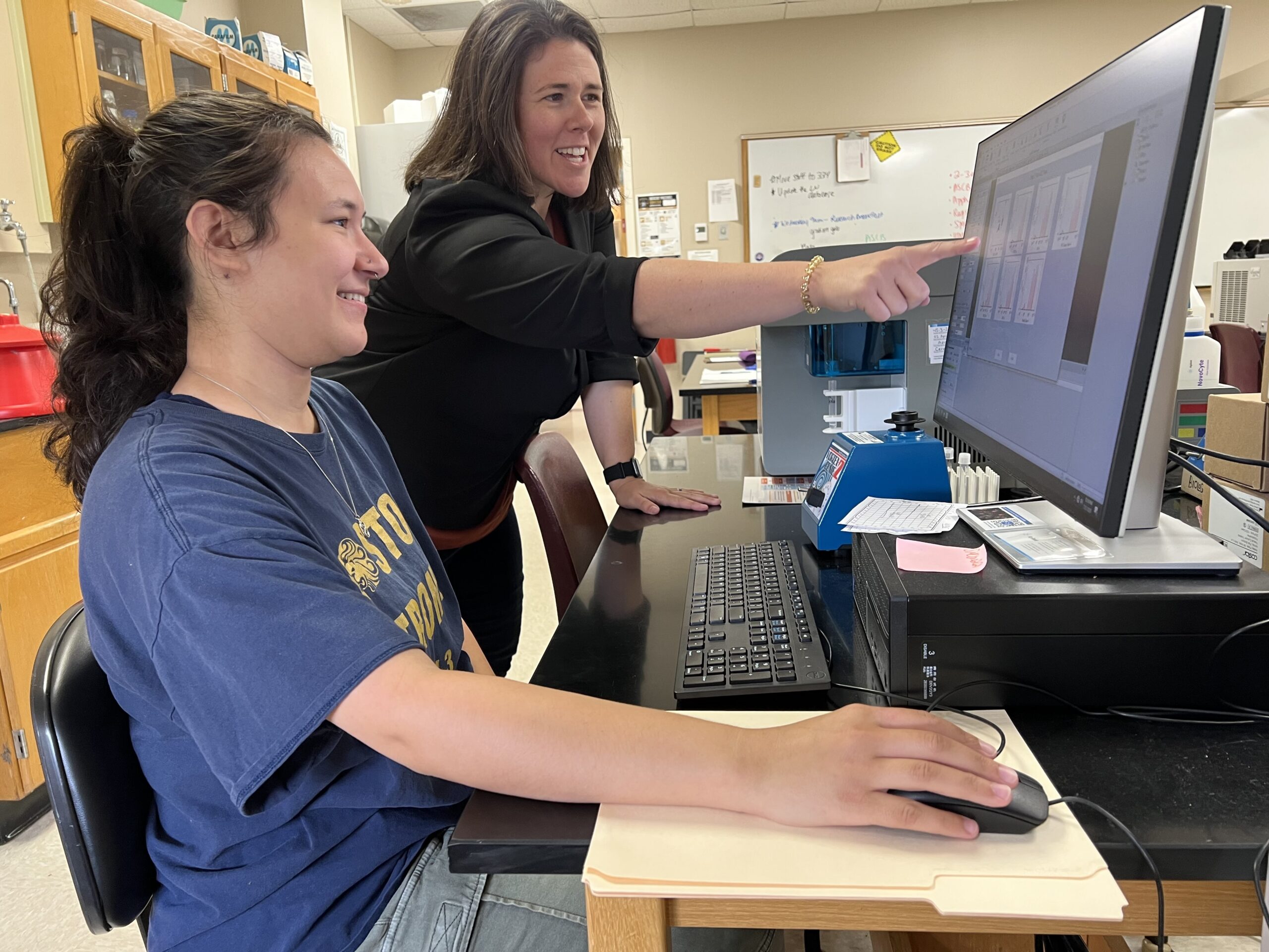 Olivia Goldfarb ’27 (left) runs a report from the flow cytometer to pinpoint specific properties within cells while Biology Professor Lyndsay Avery points at data.