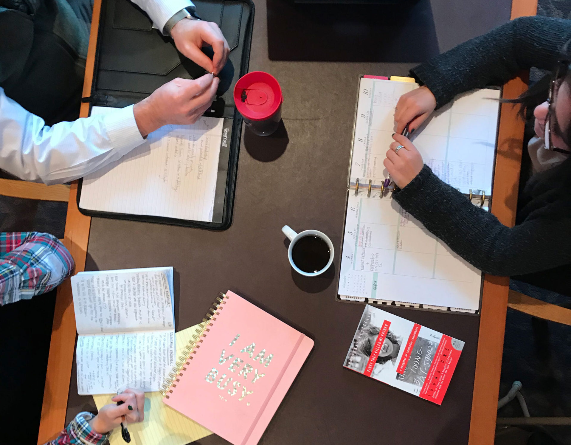 Three sets of hands work at a table with a computer and notebooks.