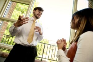 A student wearing a nice shirt and tie speaks to a second person at Saint Michael's College.