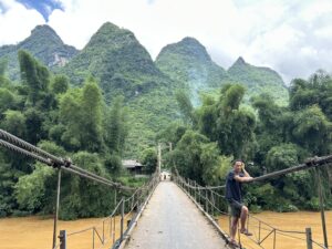 A man standing and looking, not at the beautiful mountains surrounding them, but the brown water under the bridge.