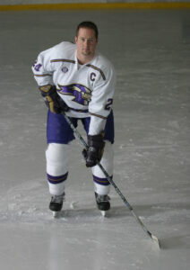 Saint Michael's College hockey player stands on the ice rink holding a hockey stick.