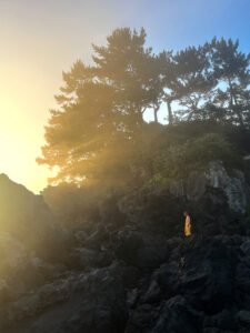 Woman in yellow stands on dark rock at a serene local-only snorkeling spot on Jeju Island, South Korea
