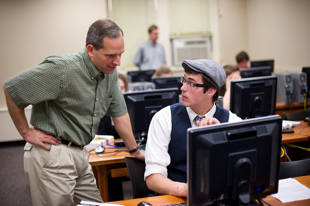 faculty member looks over student's shoulder at work on a computer screen