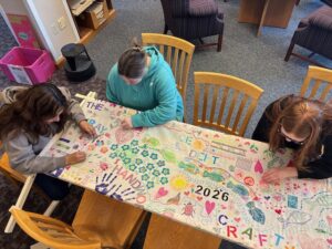 Students embroider a long piece of cloth.