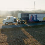 A traveling museum in a retrofitted tractor trailer truck drives down a roadway.