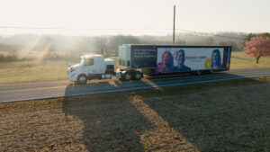 A traveling museum in a retrofitted tractor trailer truck drives down a roadway.