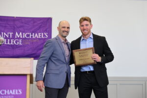 Two men pose, smiling, with a plaque during an awards ceremony. 