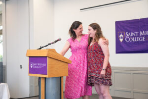 Two women embrace at the podium during an awards ceremony.