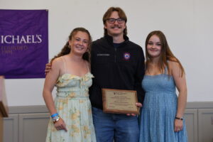 A young man holding an awards plaque poses with two young women during an awards ceremony.