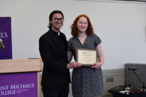 Saint Michael's College priest poses with a female student holding an award plaque. 