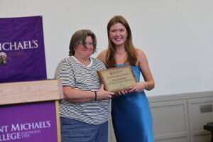 Two women pose for a photo while holding an awards plaque. 