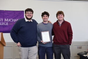 Three young men, one in the middle with a plaque, pose for a photo during an awards ceremony.