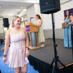 A young woman smiles as she approaches the stage to accept an award during an awards ceremony.