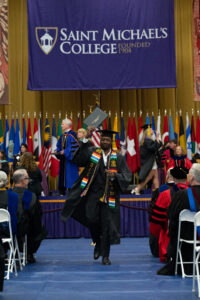 A graduate in a cap and gown holds up his diploma while walking away from a stage.