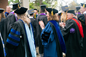 Professors in regalia applaud students as they head to graduate.