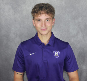 A student in a purple shirt poses in front of a gray backdrop during an Athletics photoshoot.