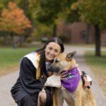 A graduate poses with a dog wearing a Saint Michael's College bandana.