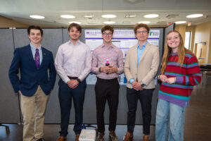Students stand in front of their presentation board during academic symposium