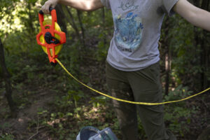 A student stretches bright yellow transect tape in the Saint Michael's College Natural Area.