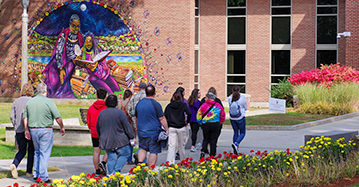 A group of students and parents on a campus tour with a mural in the background and flowers in foreground.