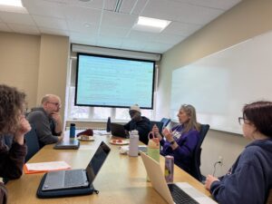 A group of students and faculty meet at a table to discuss research.