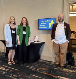 Three Saint Michael's College professors pose for a photo next to a sign that says "New England Political Science Association" 